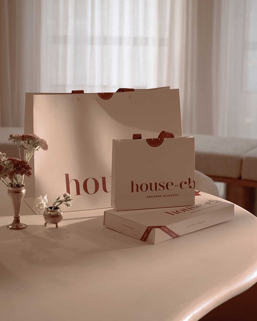 Branded packaging, shopping bags, and floral arrangements displayed on a sculptural table in a softly lit interior