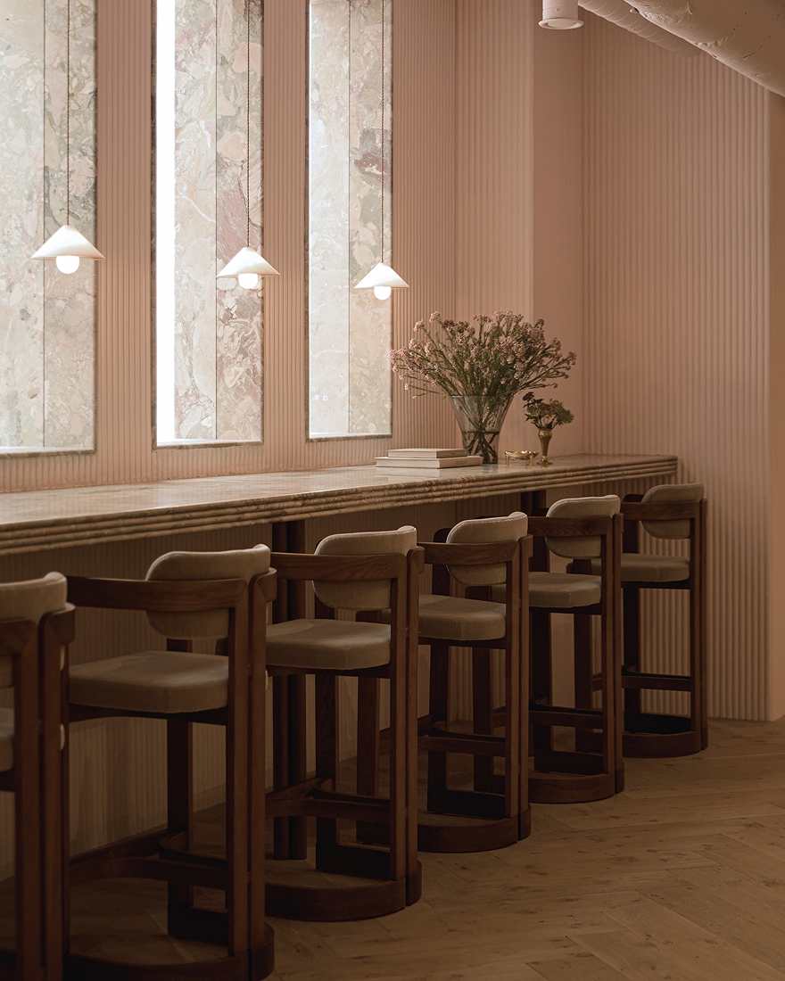 Wooden bar stools lined along a marble counter with pendant lights and floral arrangement in a modern interior