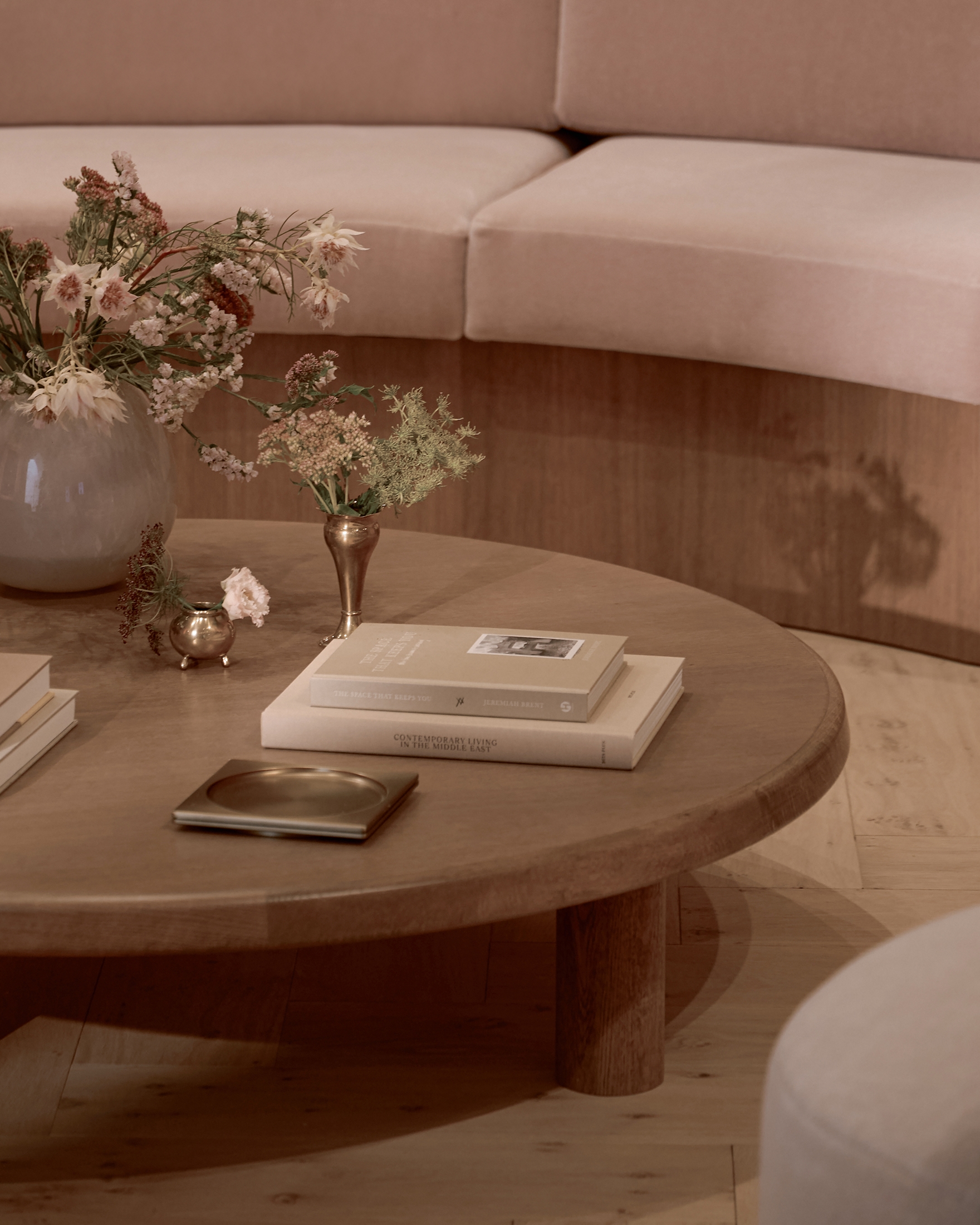 Round wooden coffee table with books, floral arrangements, and decorative objects in a warm contemporary interior