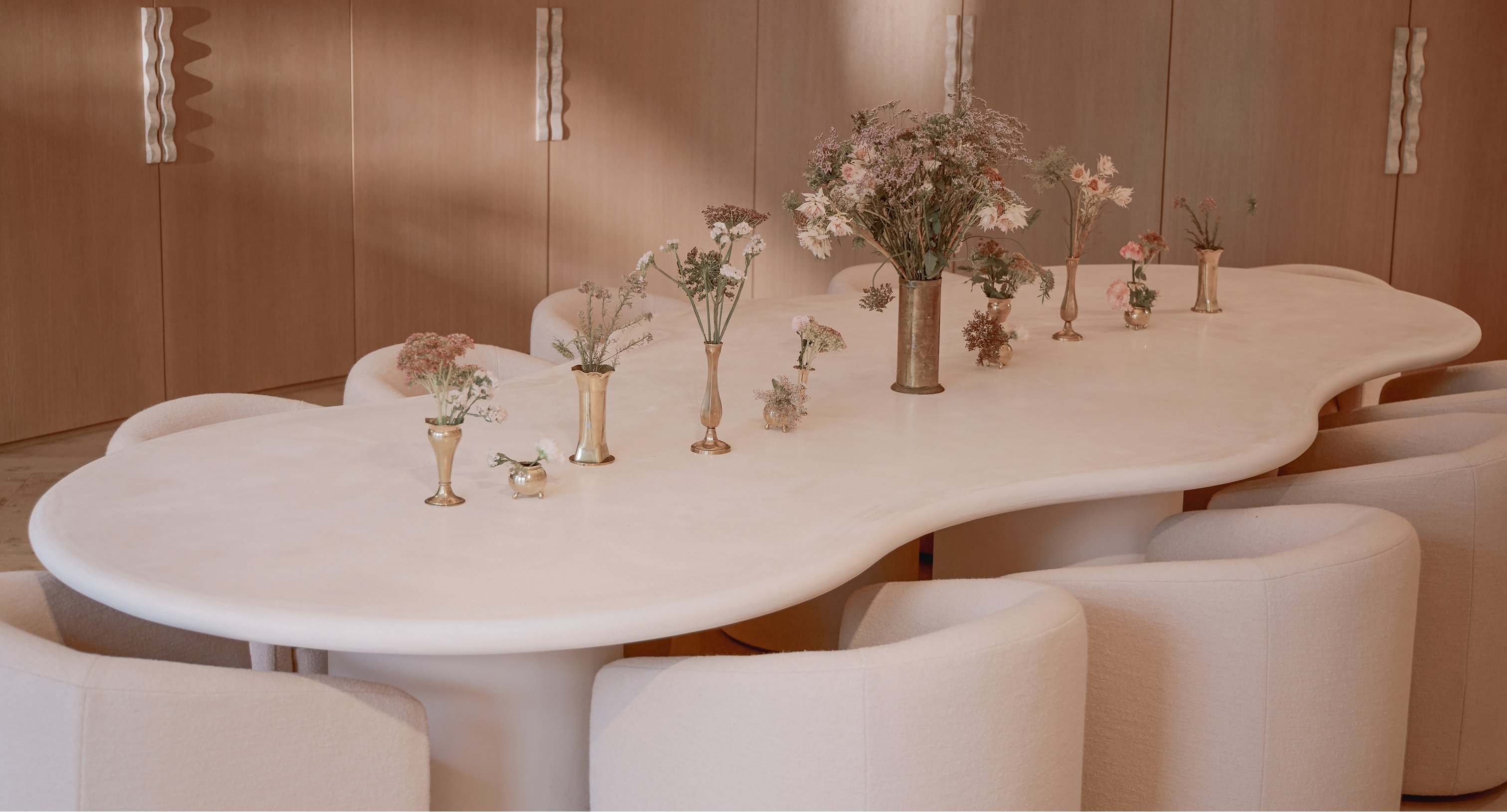 Large sculptural table surrounded by upholstered chairs and decorated with floral arrangements