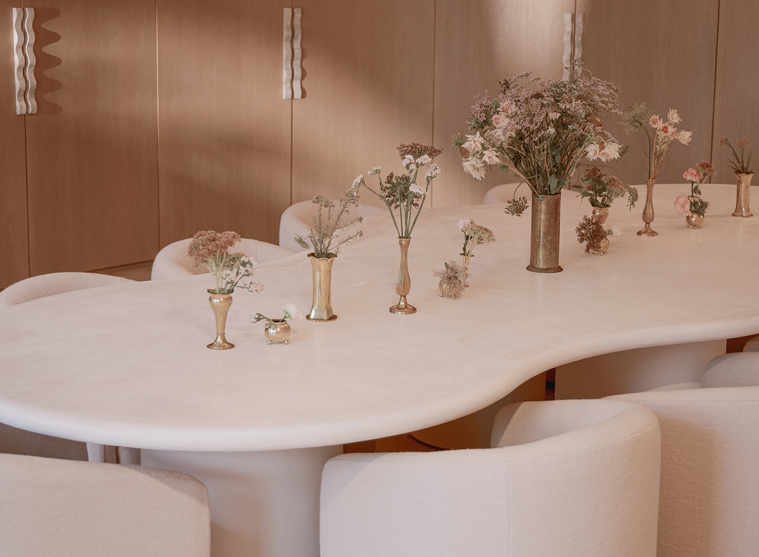 Large sculptural table surrounded by upholstered chairs and decorated with floral arrangements