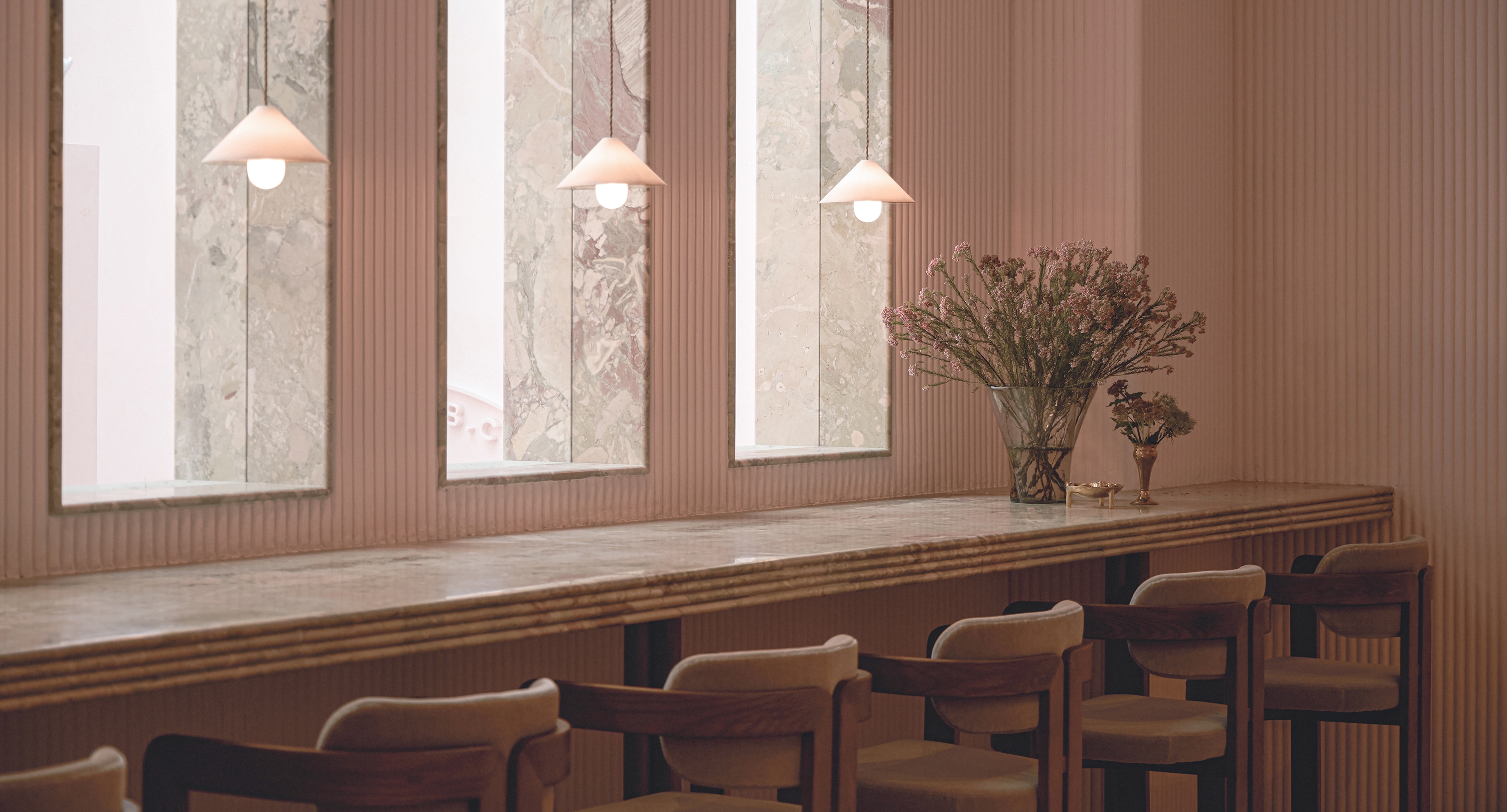 Long marble counter with wooden chairs, pendant lights, and floral arrangement in a modern interior