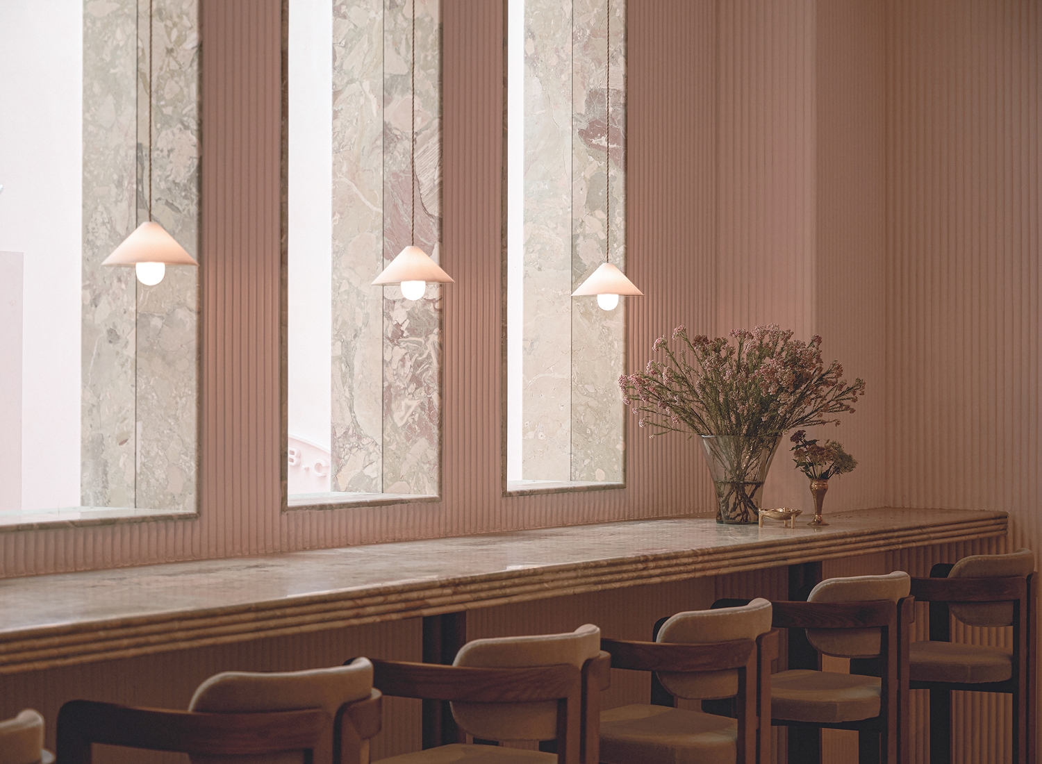 Long marble counter with wooden chairs, pendant lights, and floral arrangement in a modern interior