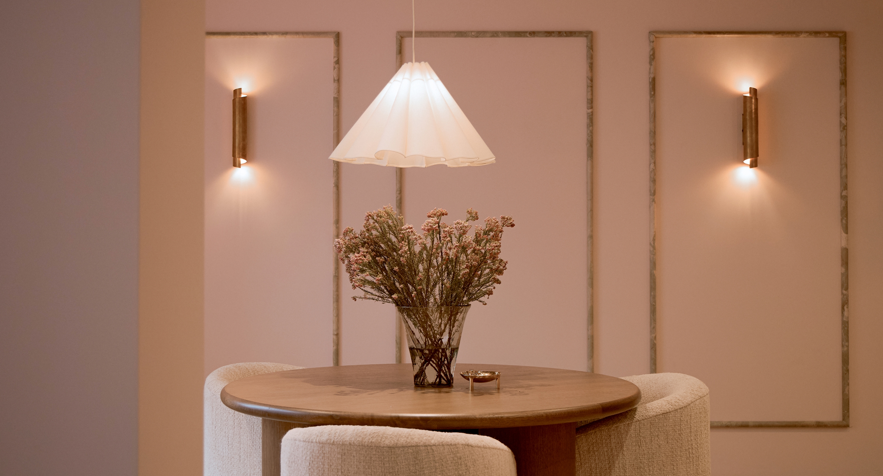 Round wooden table with upholstered seating, pendant light, and floral centerpiece in a softly lit interior