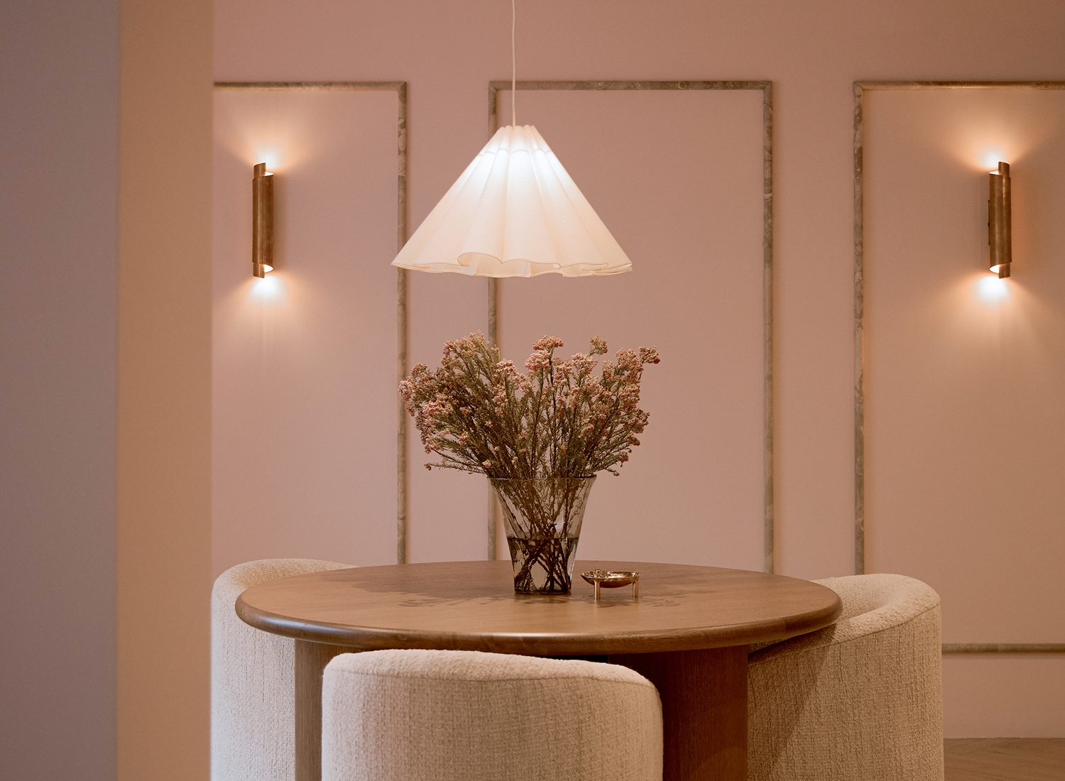 Round wooden table with upholstered seating, pendant light, and floral centerpiece in a softly lit interior