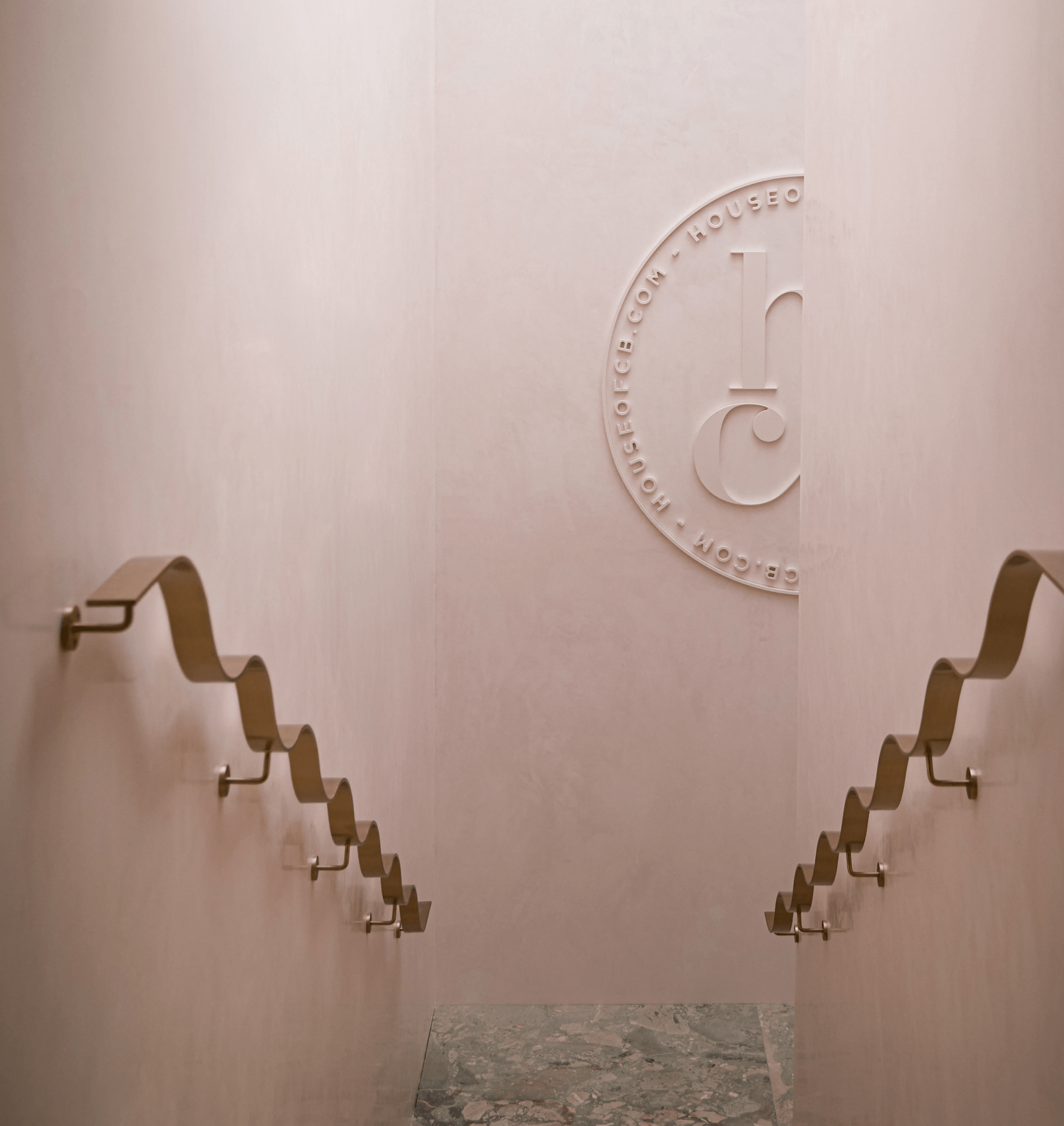 Decorative wall emblem above a marble floor, framed by sculptural metal wall hooks in a minimalist interior