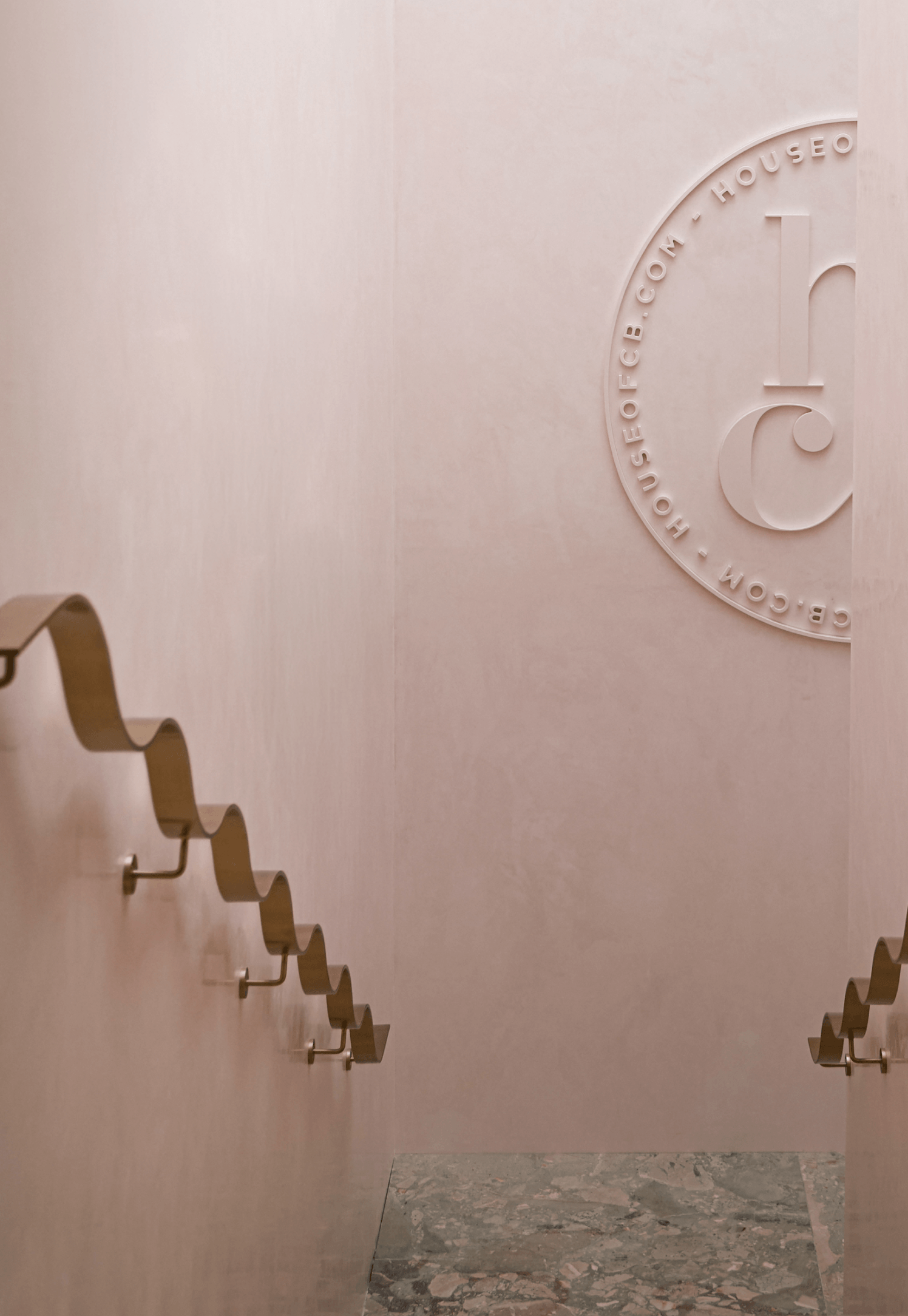 Decorative wall emblem above a marble floor, framed by sculptural metal wall hooks in a minimalist interior